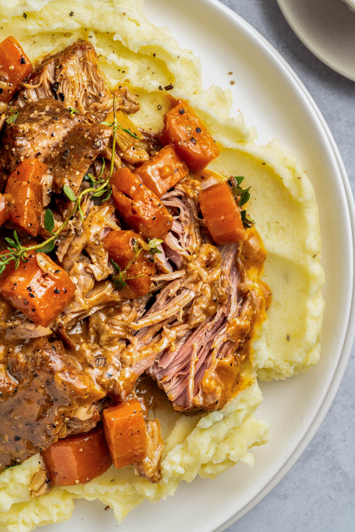 A dinner plate full of shredded braised pork shoulder, carrots, and gravy over mashed potatoes.