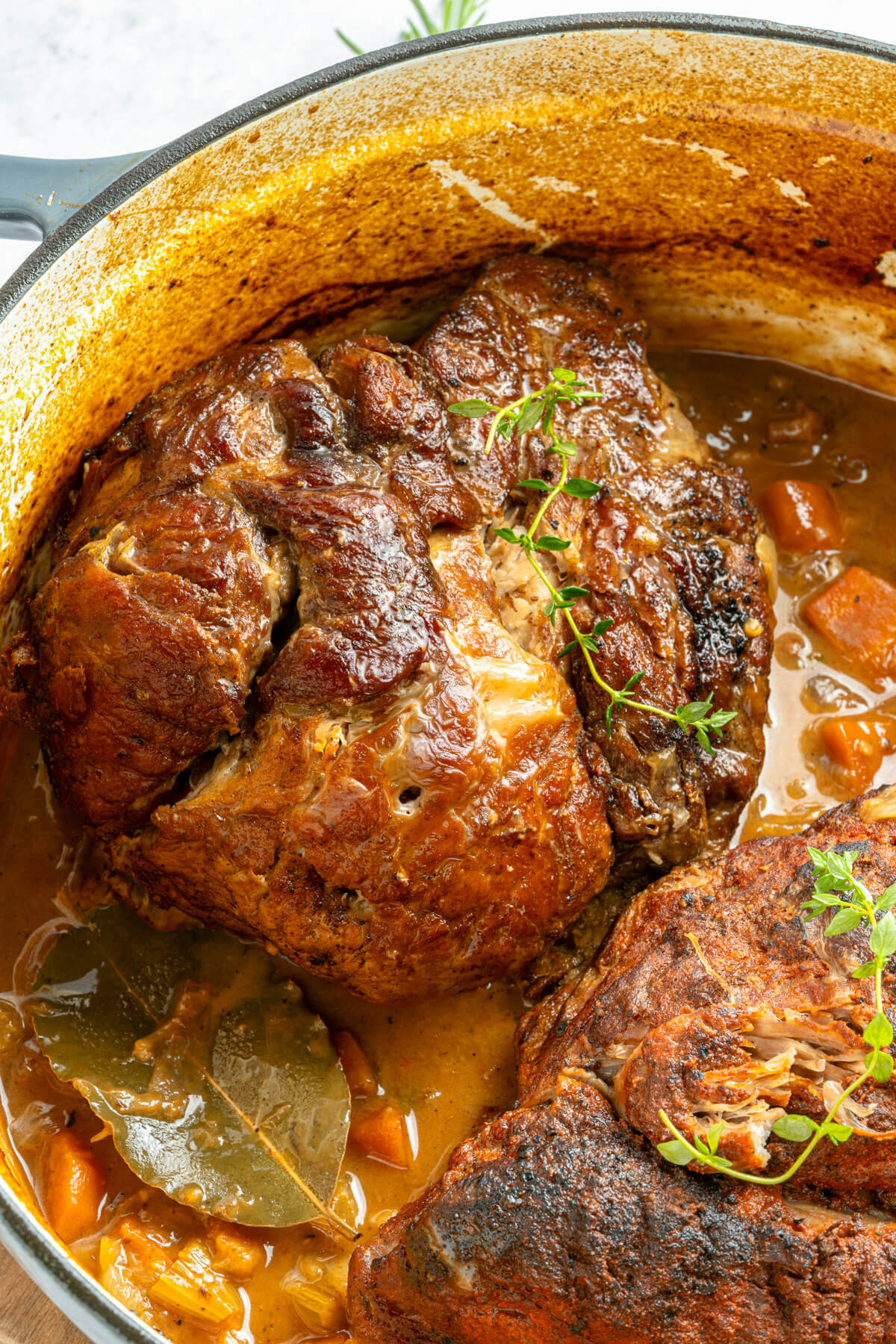 A Dutch oven containing two fork tender pieces of braised pork should in braising liquid.