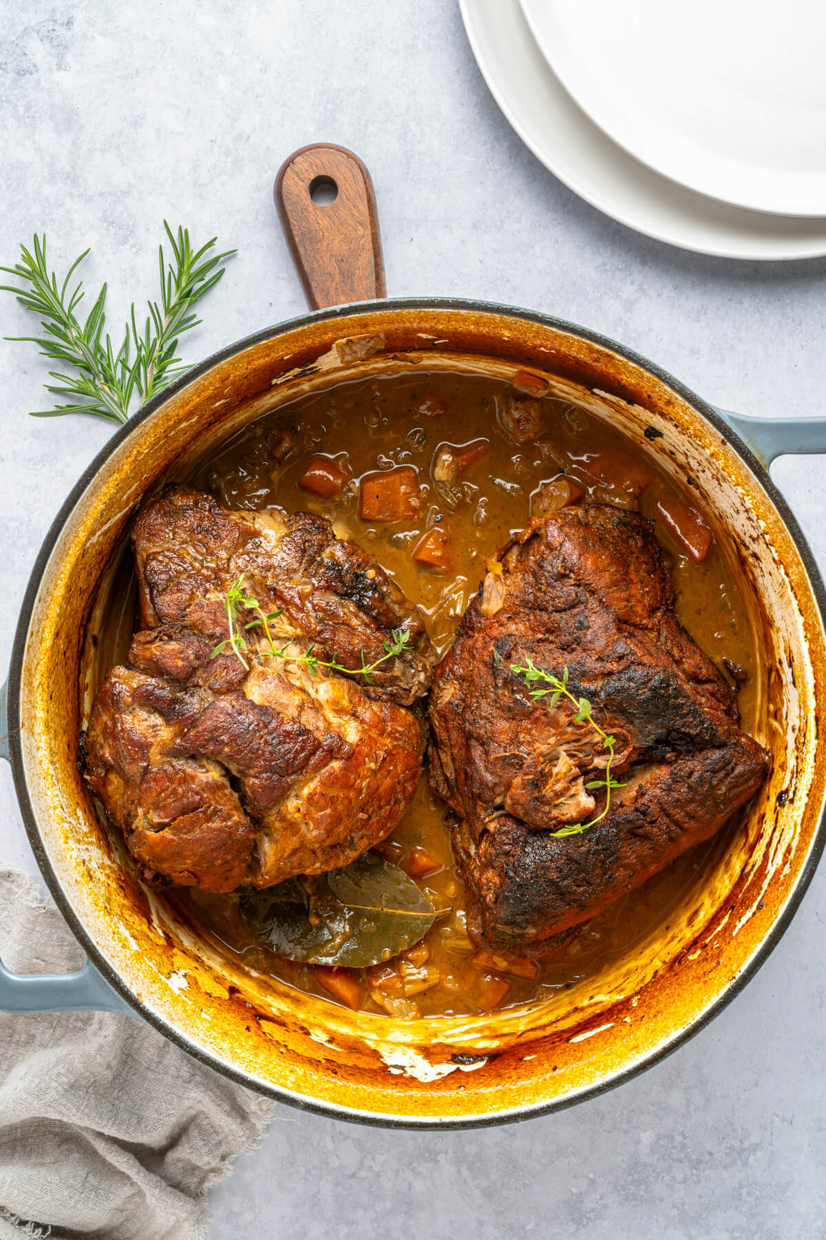 A Dutch oven containing two fork tender pieces of braised pork shoulder in braising liquid.