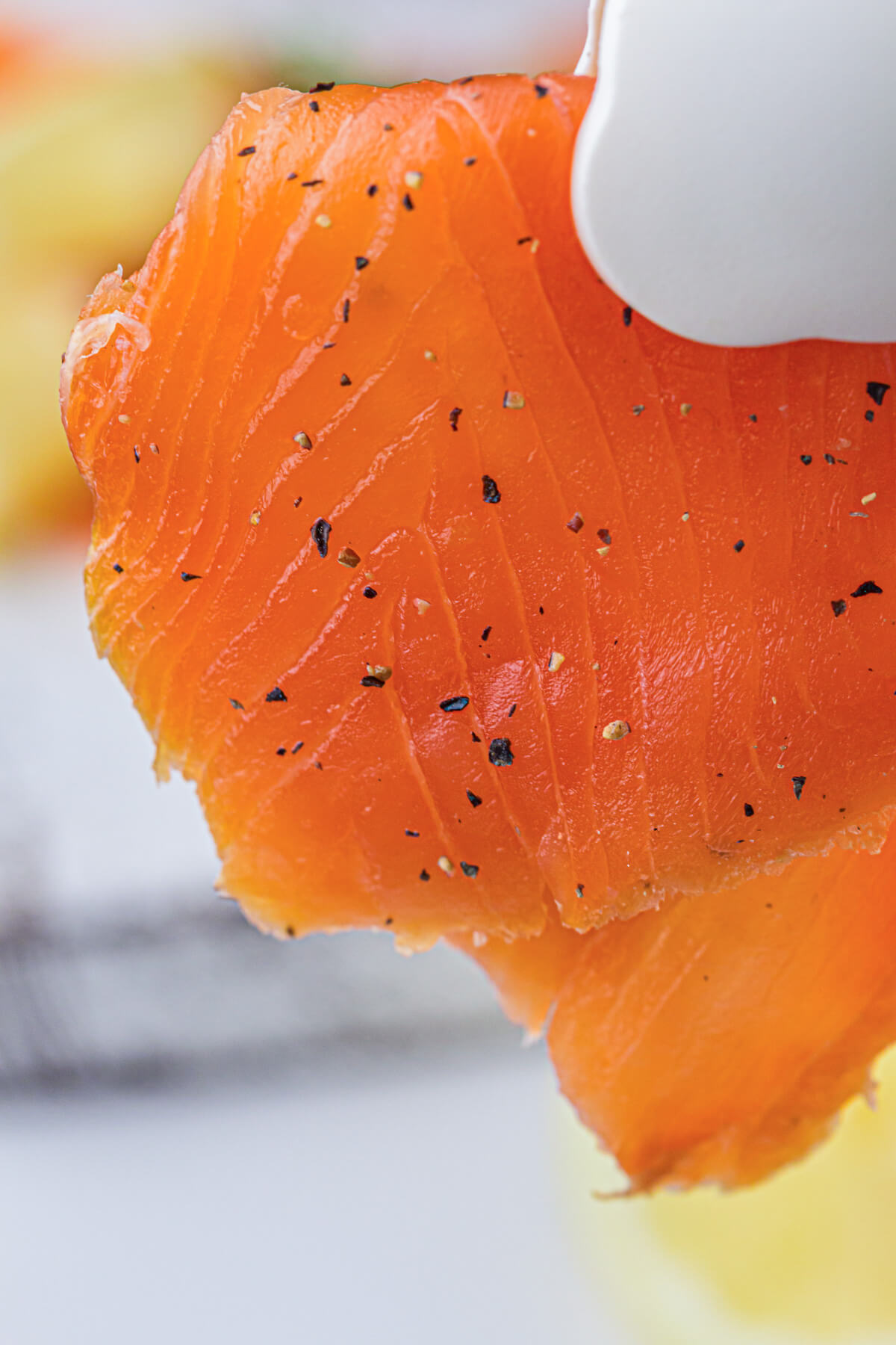 A pair of tongs holds up a thin piece of cold smoked salmon filet.