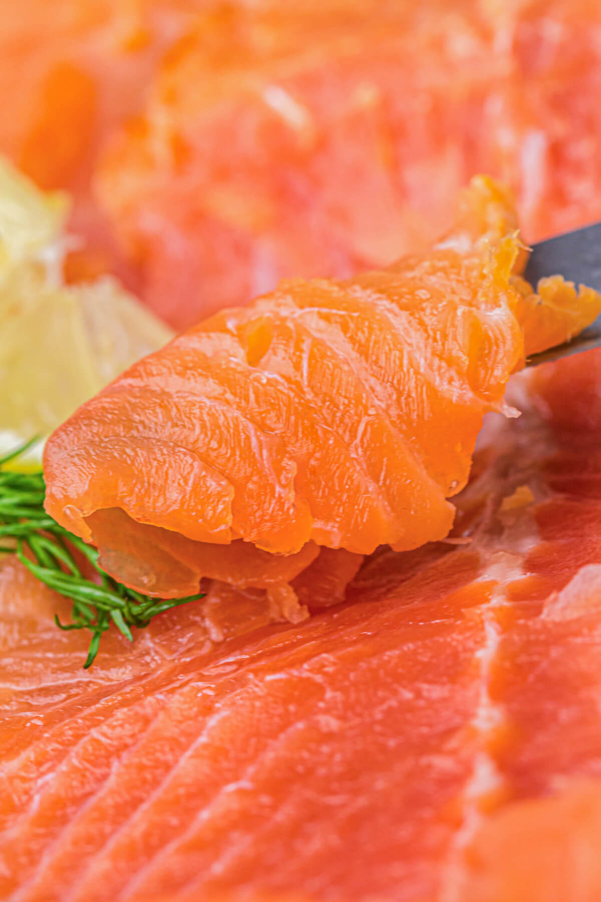 A sharp knife holds up a thin piece off of a whole cold smoked salmon filet.