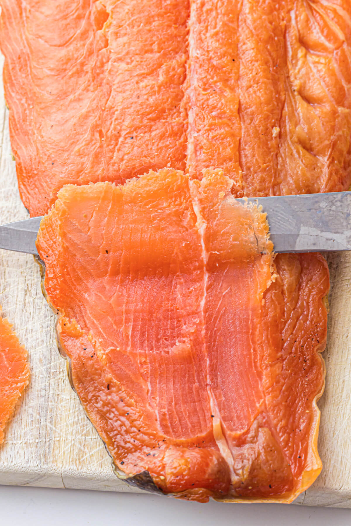 A sharp knife slices a thin piece off of a whole cold smoked salmon filet.