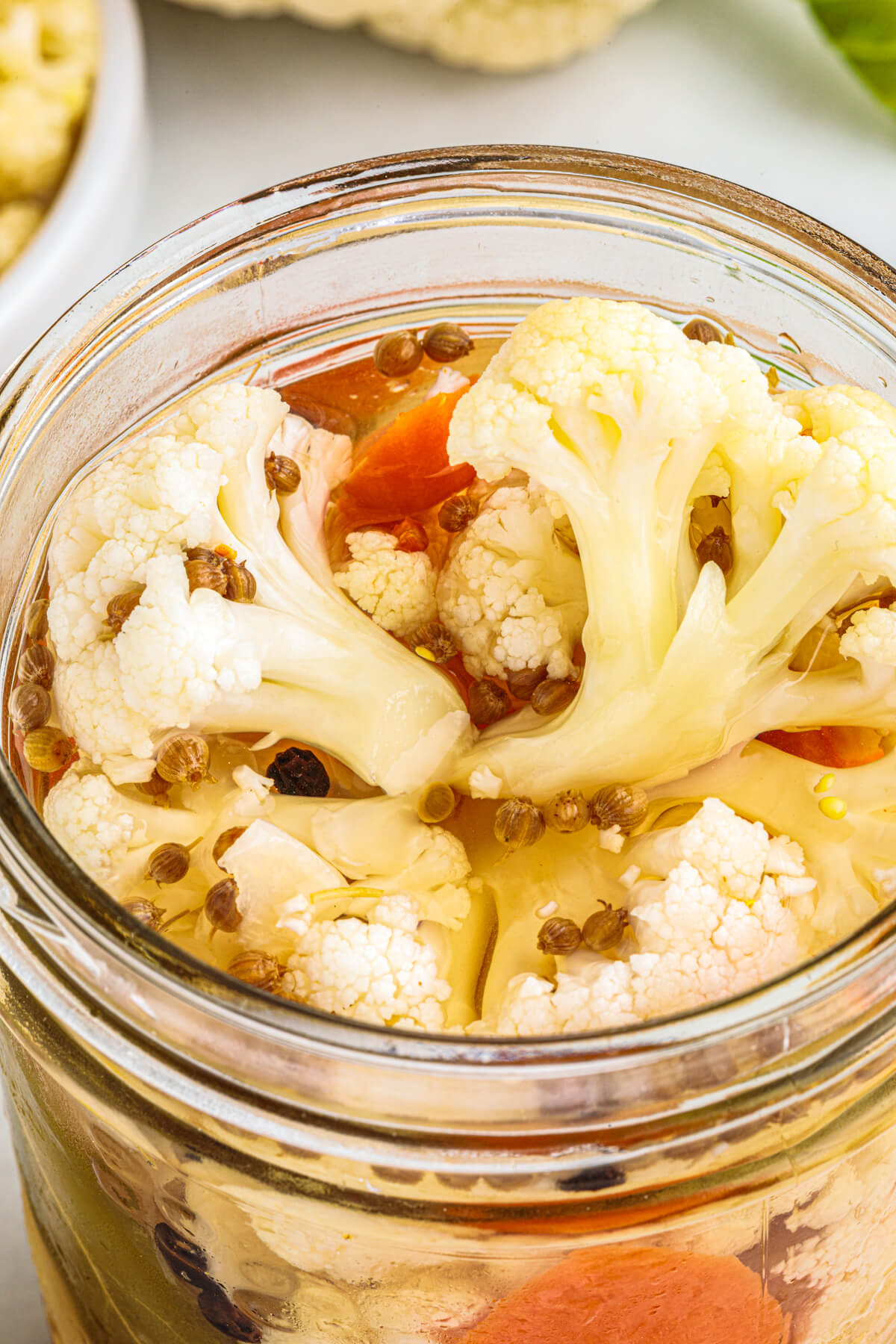 Close picture of a glass pint jar containing pickled cauliflower with carrots and pickling spices.