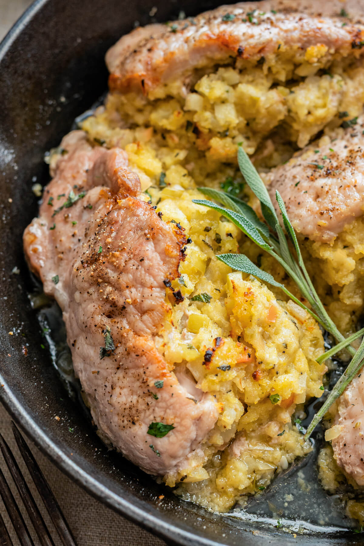 A perfectly cooked stuffed pork chop in a cast iron skillet garnished with fresh sage.