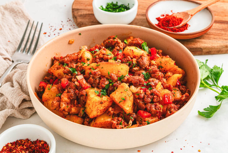 A breakfast bowl filled with vibrant papas con chorizo containing red peppers, potatoes, chorizo and cilantro as garnish.