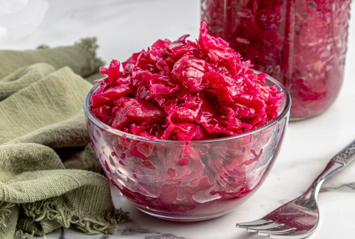 A glass bowl filled with vibrant purple fermented cabbage in front of a full jar of red cabbage sauerkraut.