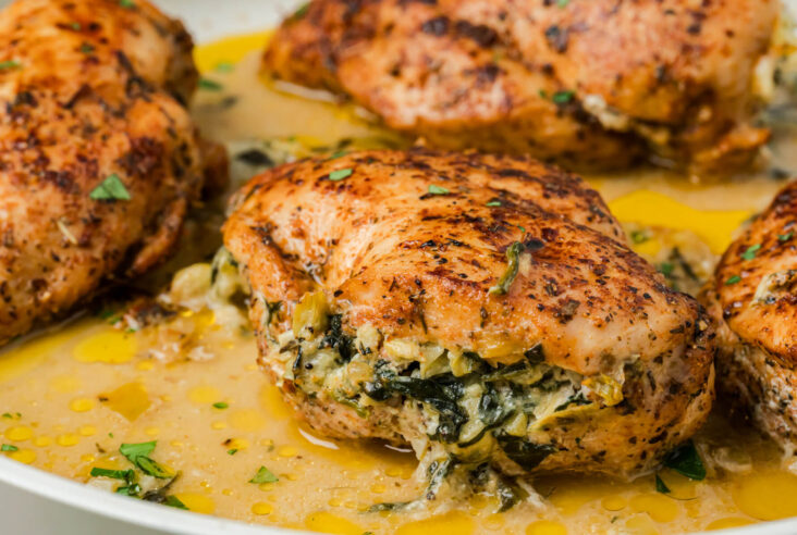 A pan filled with golden seared chicken breasts stuffed with creamy spinach and artichoke stuffing.
