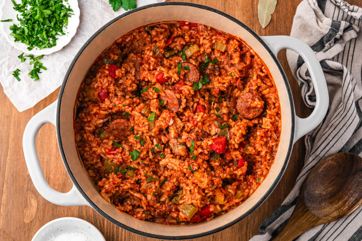 A Dutch oven full of vibrant red sausage chicken jambalaya with red and green bell peppers garnished with fresh parsley.
