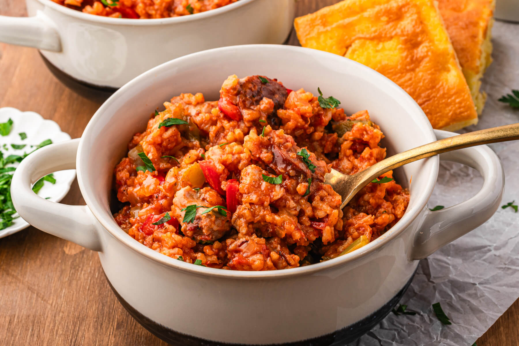 A bowl of vibrant red sausage chicken jambalaya with red and green bell peppers garnished with fresh parsley.
