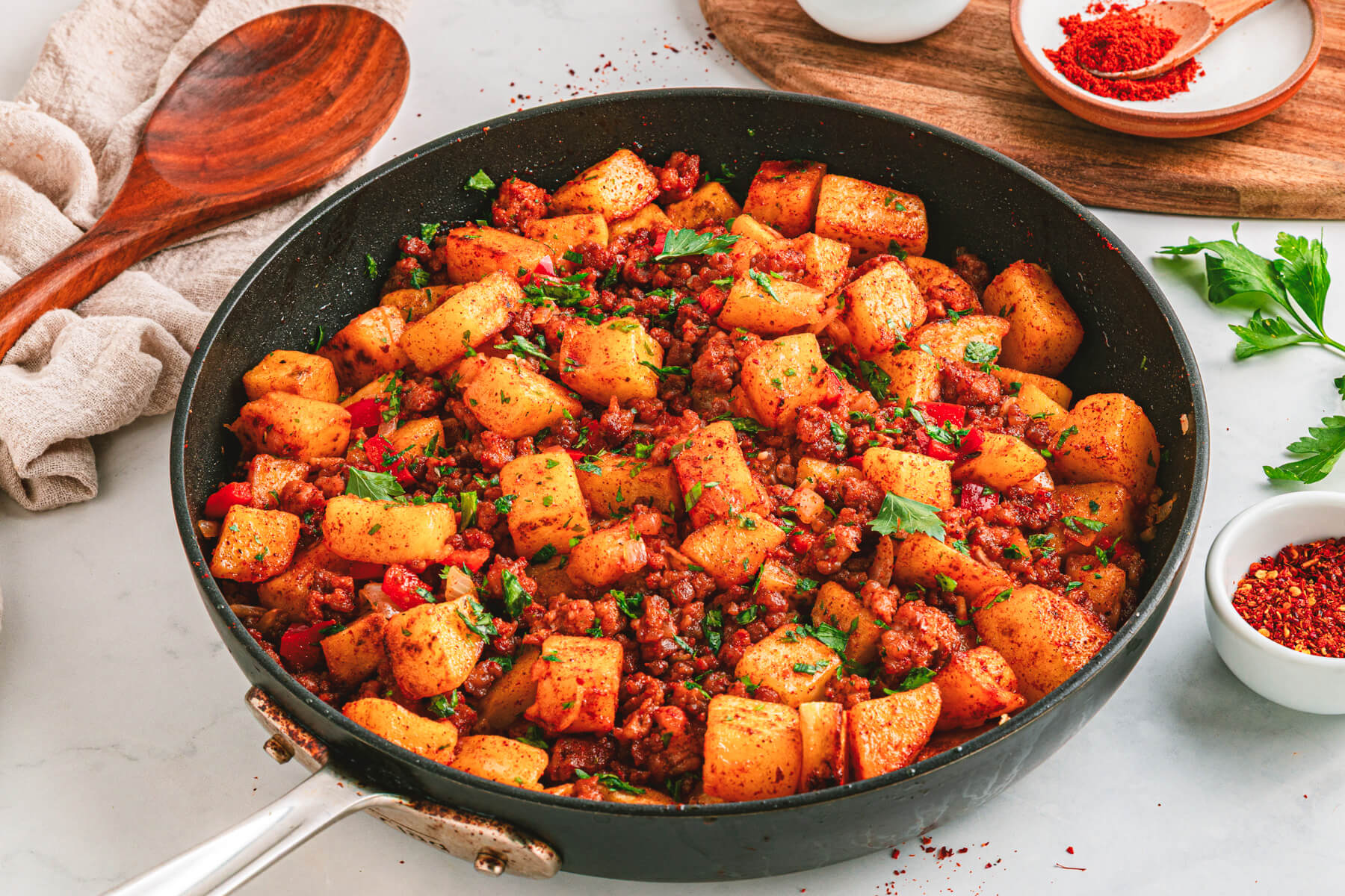 A cast iron skillet filled with vibrant papas con chorizo containing red peppers, potatoes, chorizo and cilantro as garnish.
