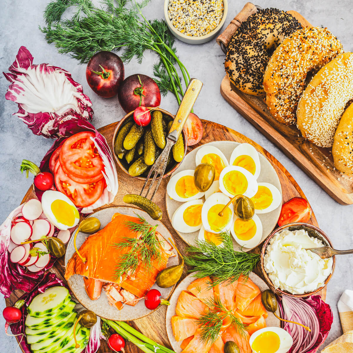 A lovely brunch table set with freshly baked bagels, soft boiled eggs, sliced smoked salmon and all the toppings for bagel brunch.