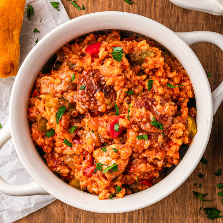 A bowl of vibrant red sausage chicken jambalaya with red and green bell peppers garnished with fresh parsley.
