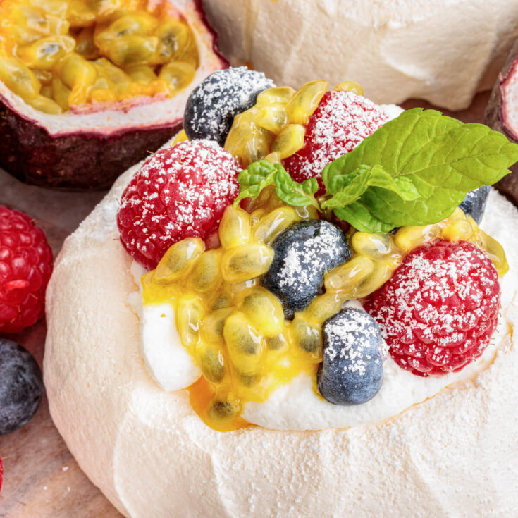 A Mini Pavlova topped with whipped cream, fresh berries, passionfruit pulp and fresh mint leaves on a serving platter.