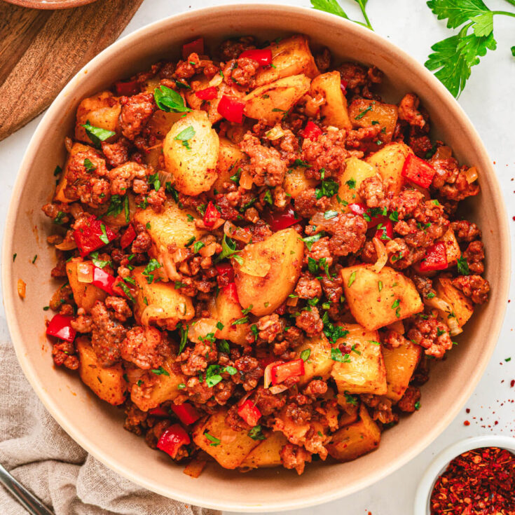 A breakfast bowl filled with vibrant papas con chorizo containing red peppers, potatoes, chorizo and cilantro as garnish.