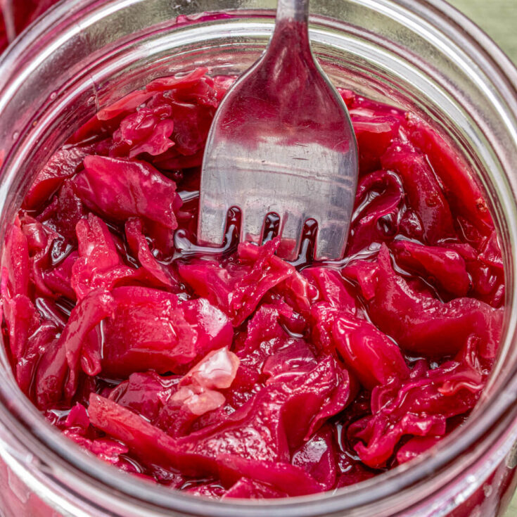 A fork in a glass jar filled with vibrant purple fermented cabbage.