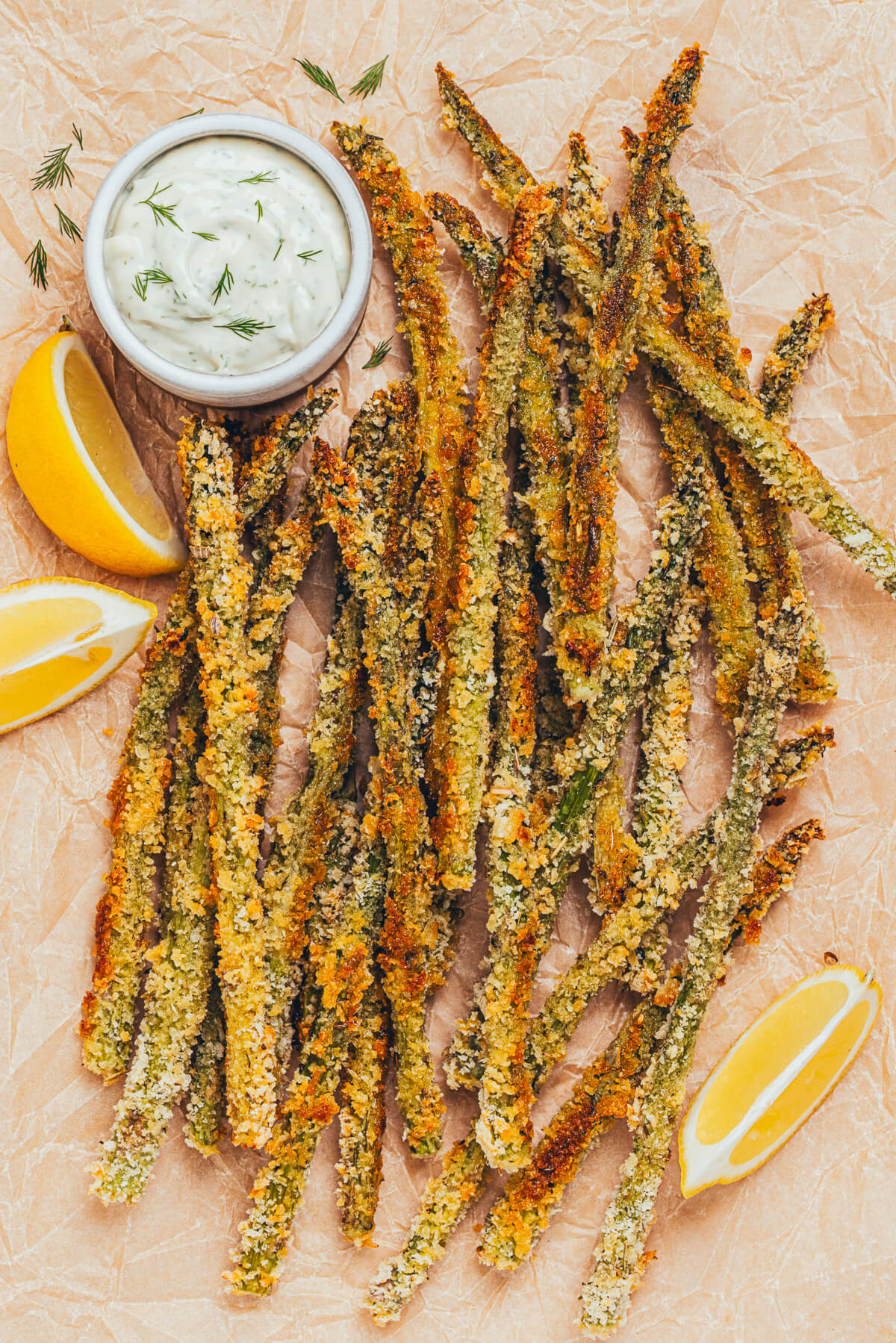 A pile of crispy golden baked asparagus fries on a parchment lined serving tray with a side of dill aioli for dipping.