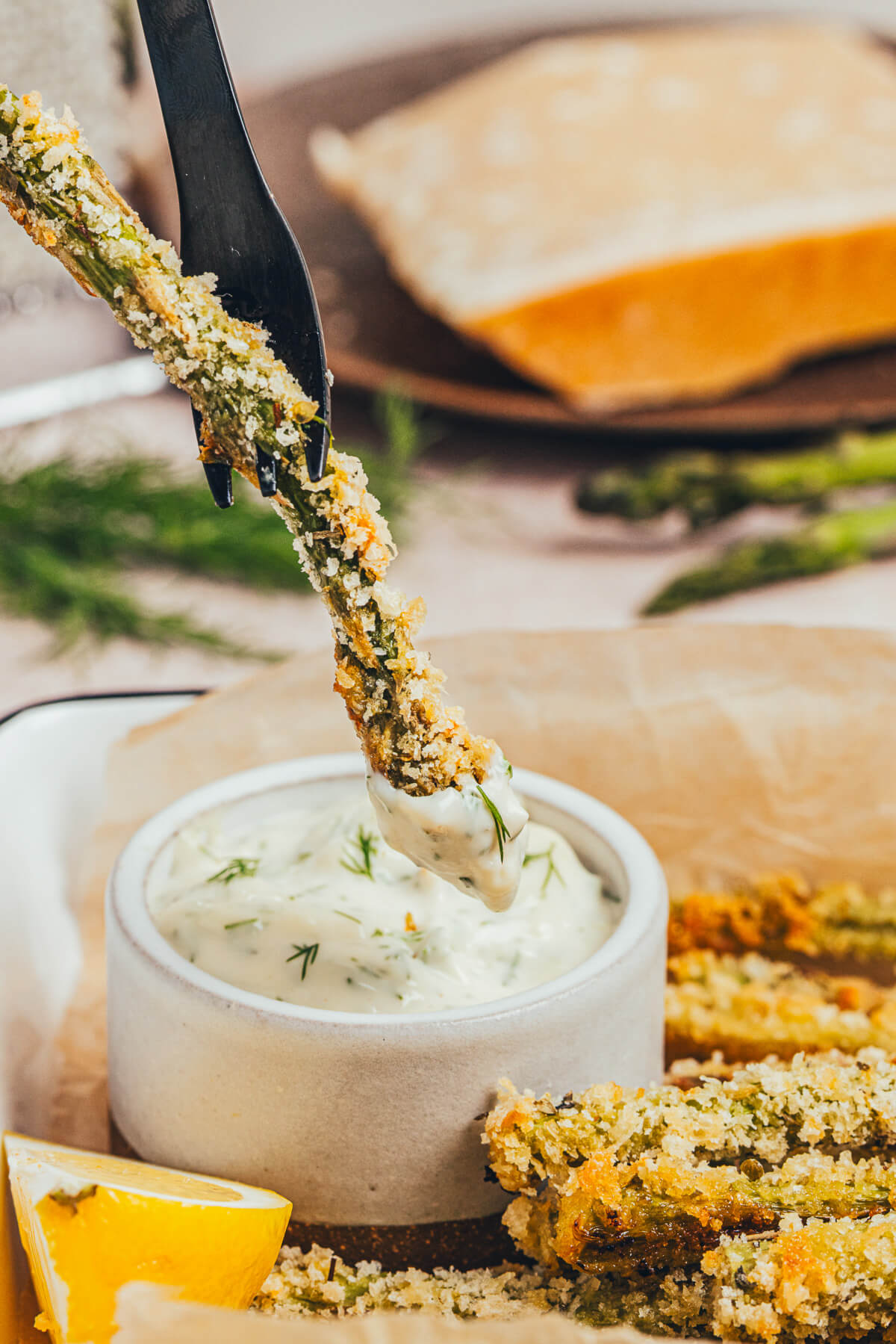 One Parmesan baked asparagus spear being dipped into a small bowl of dill aoili.