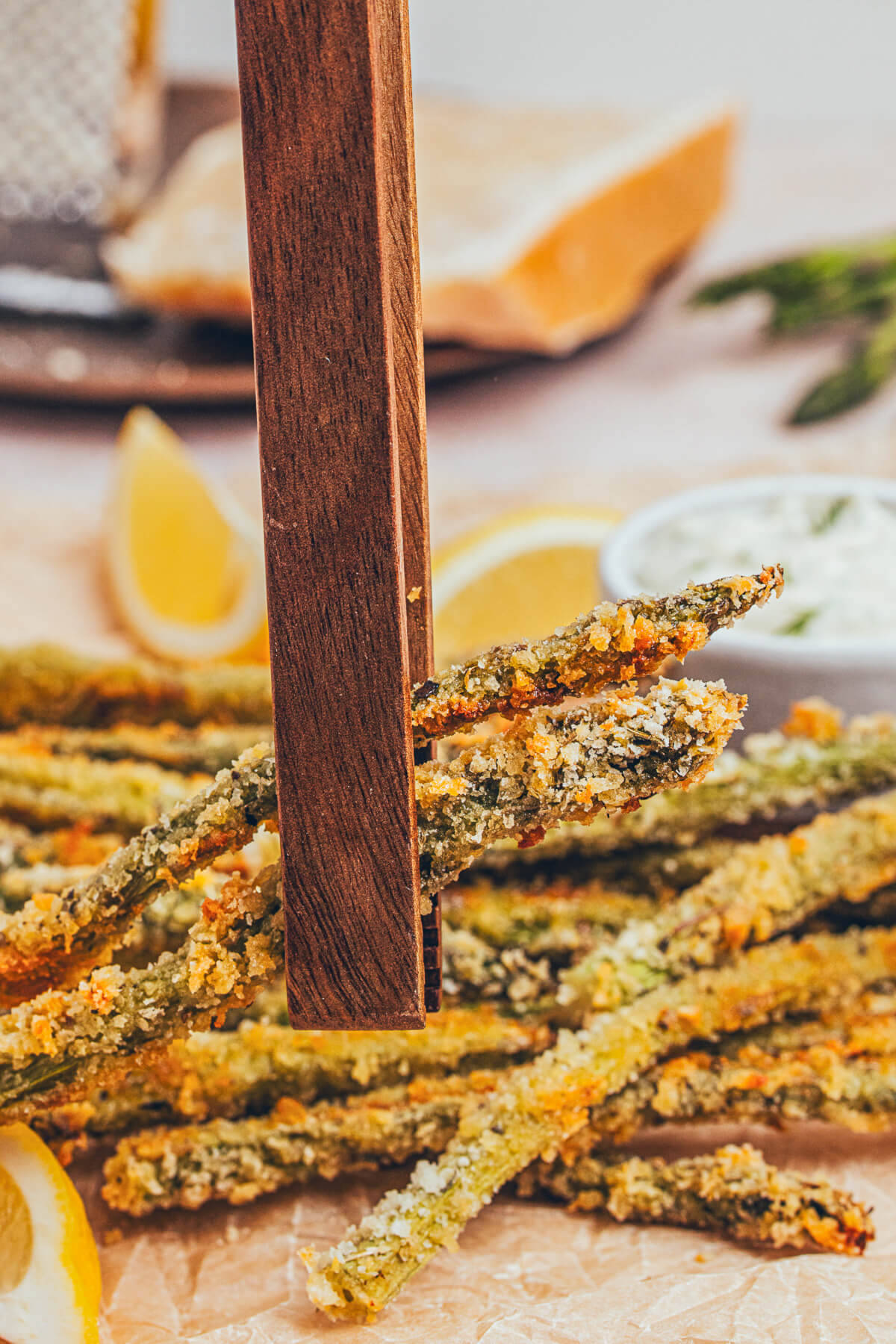 A pair of wooden tongs grabs a few golden Parmesan Baked Asparagus fries from a baking tray.