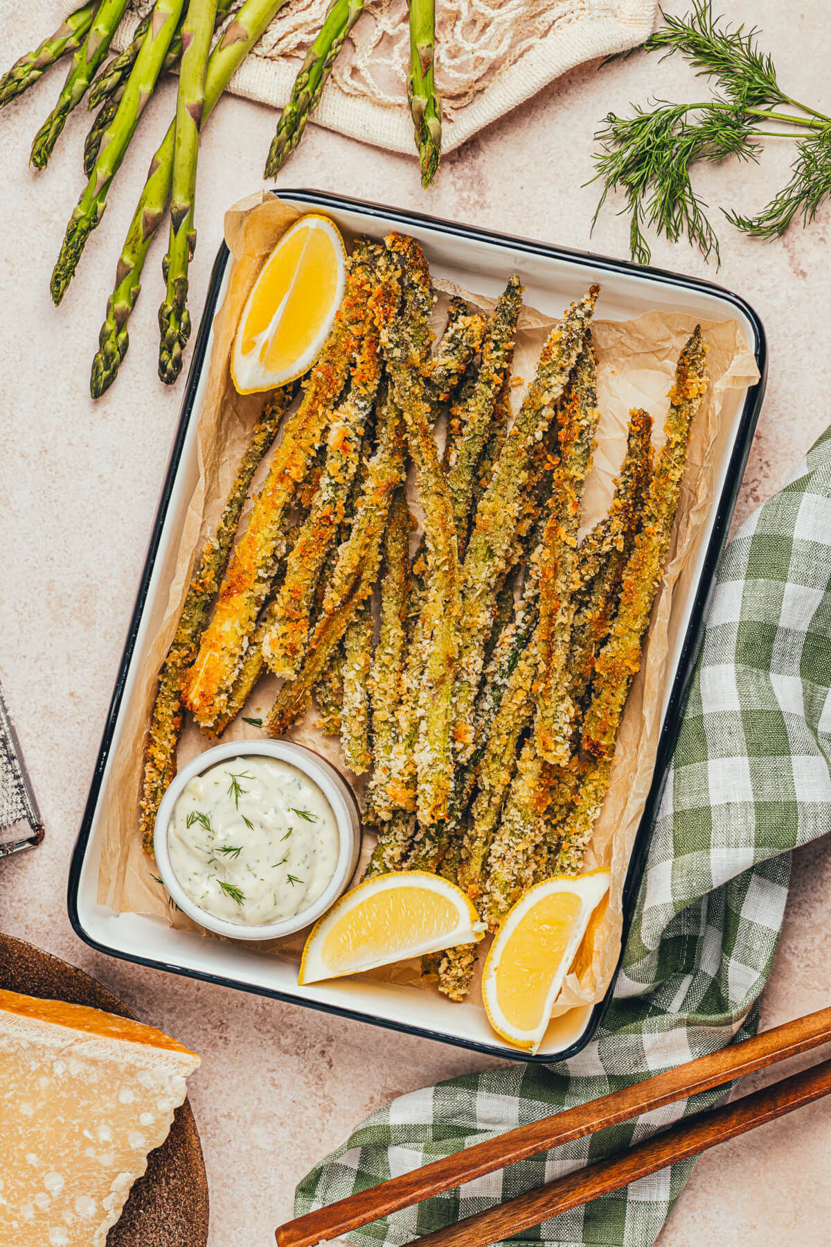 A pile of crispy golden baked asparagus fries on a parchment lined serving tray with a side of dill aioli for dipping.