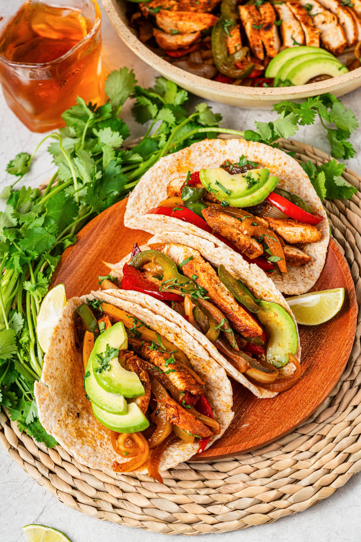 A platter of three chicken fajitas stuffed with juicy chicken, sauteed peppers, onions, and topped with sliced avocado and chopped cilantro.