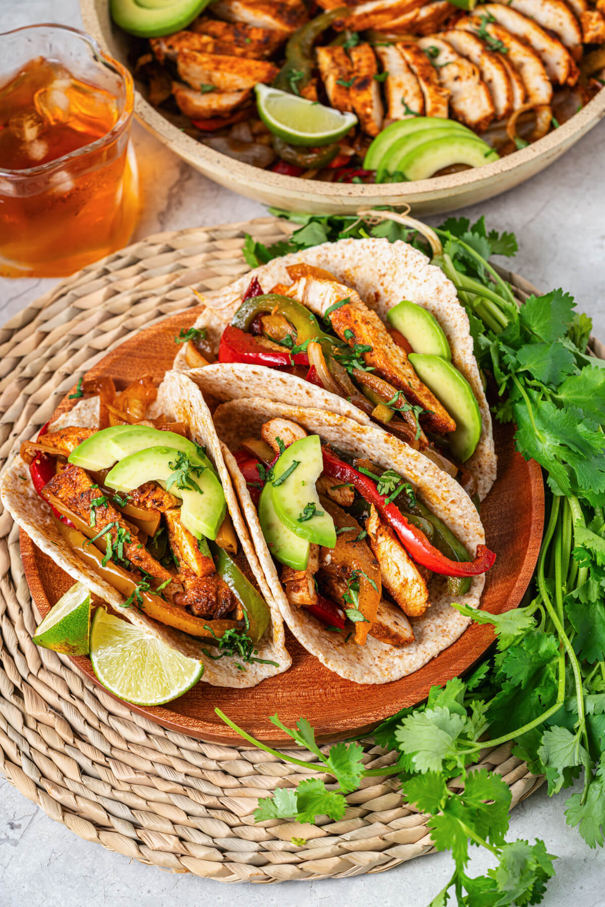 A platter of three chicken fajitas stuffed with juicy chicken, sauteed peppers, onions, and topped with sliced avocado and chopped cilantro.