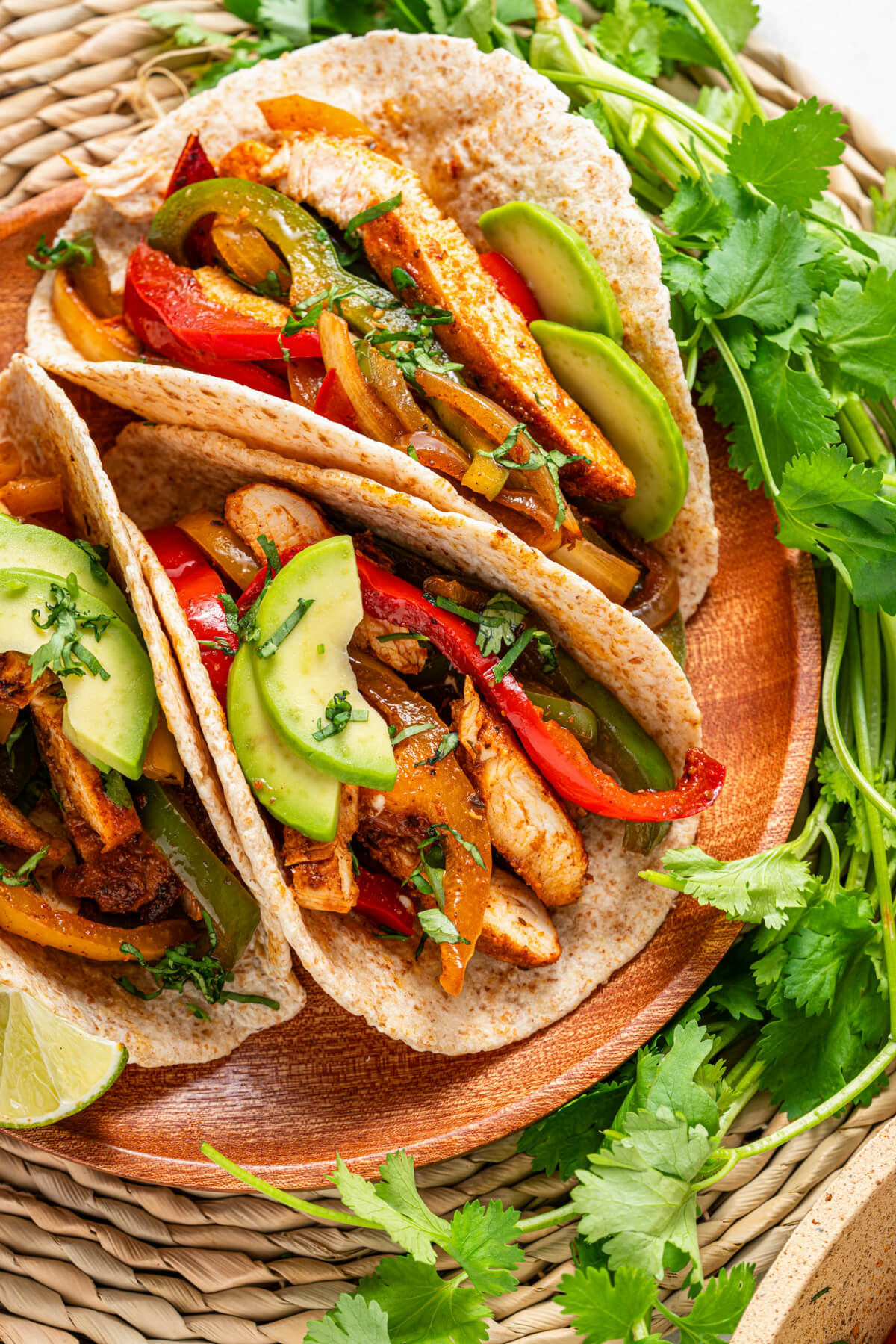 A platter of three chicken fajitas stuffed with juicy chicken, sauteed peppers, onions, and topped with sliced avocado and chopped cilantro.