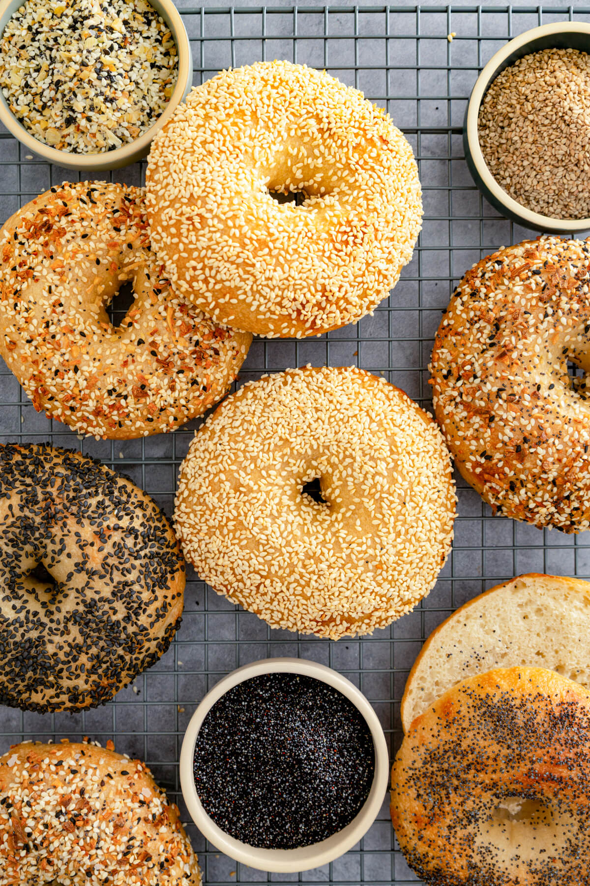 A group of freshly baked bagels with various toppings on a wire rack.