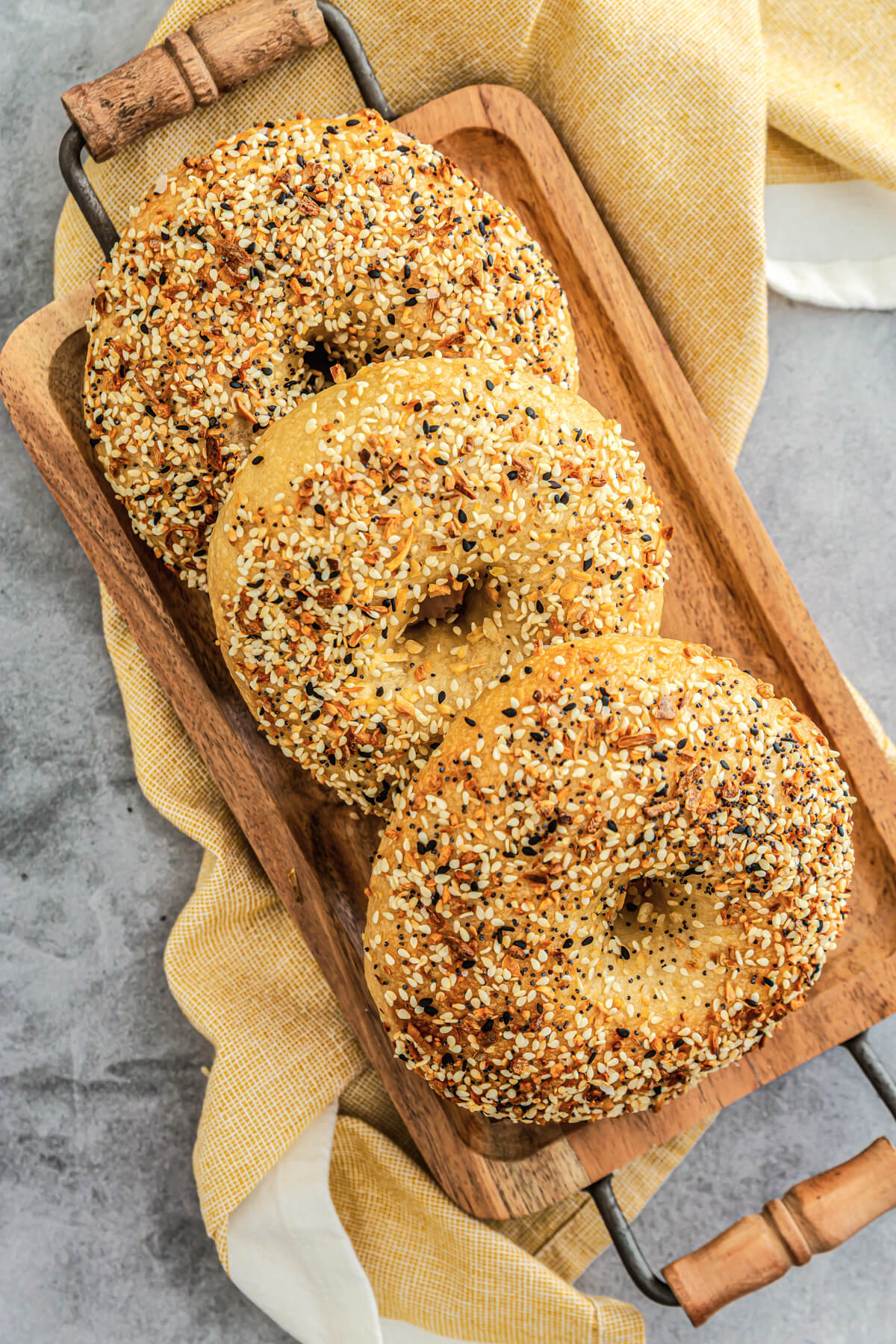 Three freshly baked everything bagels on a wooden tray.