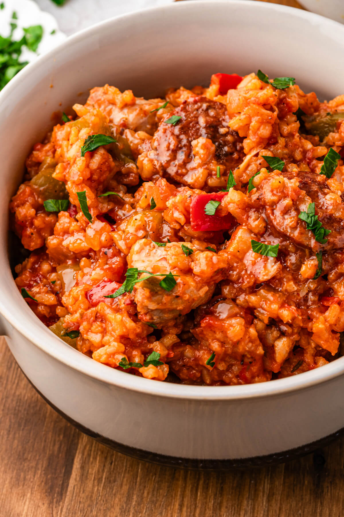 A bowl of vibrant red sausage chicken jambalaya with red and green bell peppers garnished with fresh parsley.