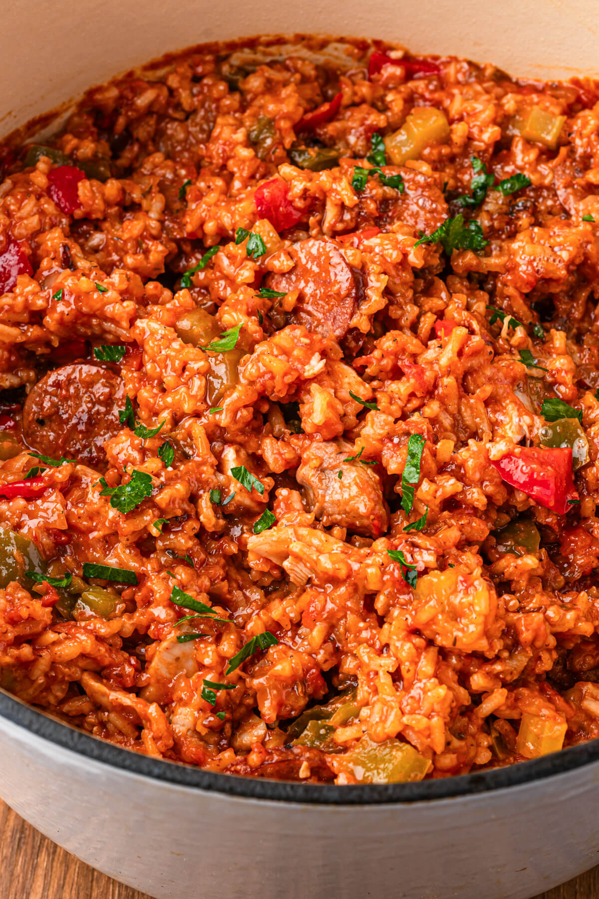 A Dutch oven full of vibrant red sausage chicken jambalaya with red and green bell peppers garnished with fresh parsley.