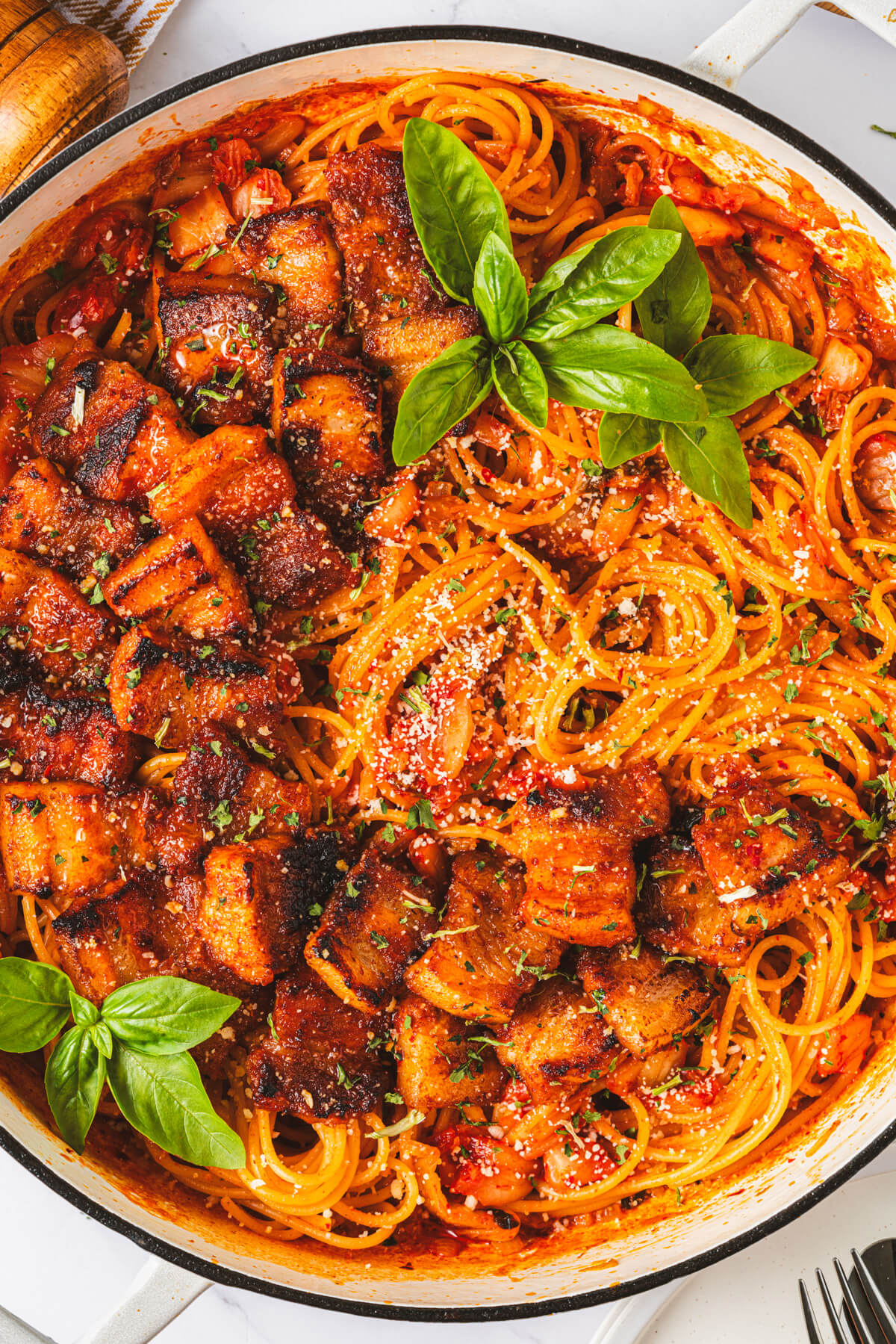 A Dutch oven filled with vibrant red Kimchi Pasta dotted with caramelized pork belly and fresh basil leaves. 