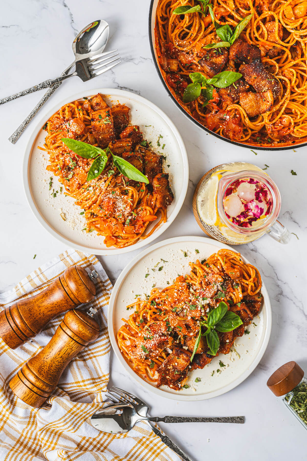 White dinner filled with Kimchi Pasta and pork belly expertly rolled into a neat line then topped with Parmesan cheese and fresh basil leaves.