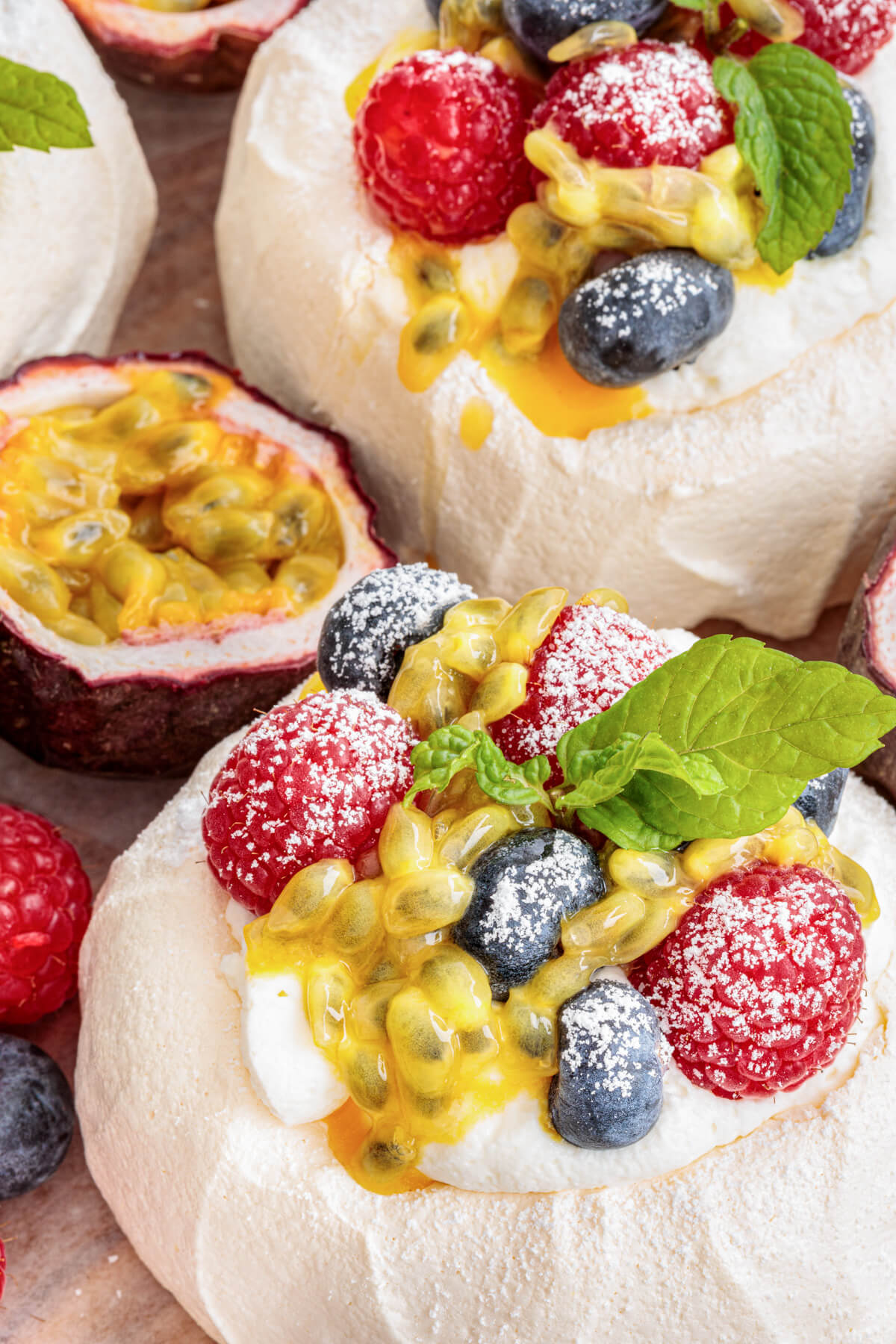 Two Mini Pavlovas topped with whipped cream, fresh berries, passionfruit pulp and fresh mint leaves on a serving platter.