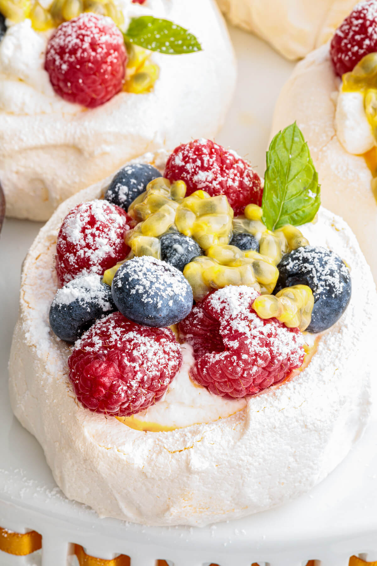 Two Mini Pavlovas topped with whipped cream, fresh berries, passionfruit pulp and fresh mint leaves on a serving platter.