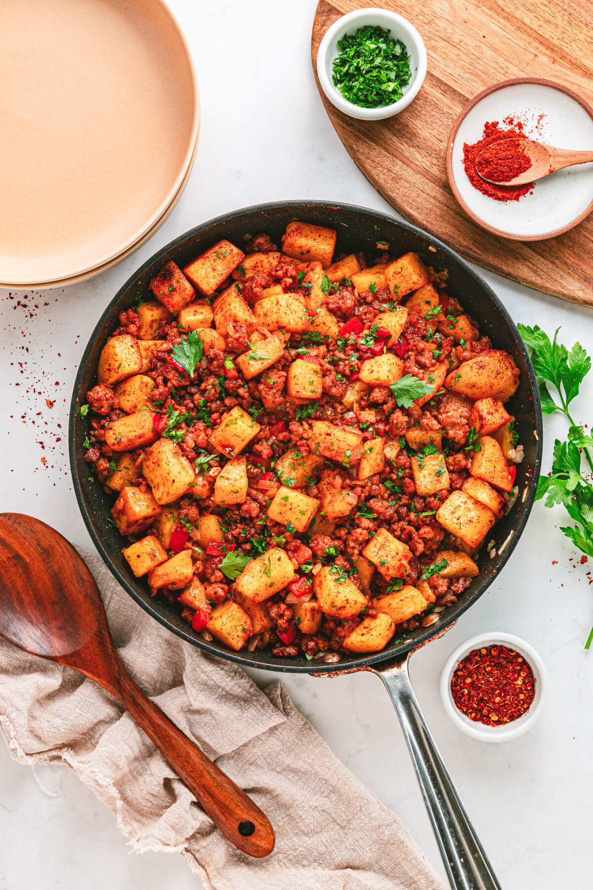 A cast iron skillet filled with vibrant papas con chorizo containing red peppers, potatoes, chorizo and cilantro as garnish.