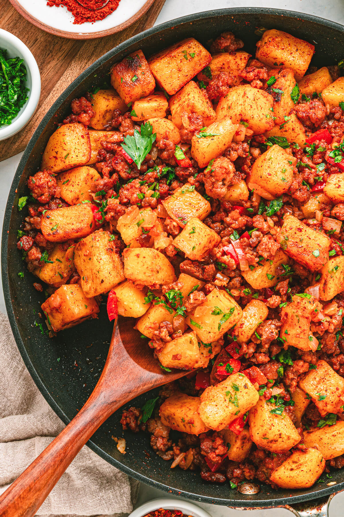 A cast iron skillet filled with vibrant papas con chorizo containing red peppers, potatoes, chorizo and cilantro as garnish.