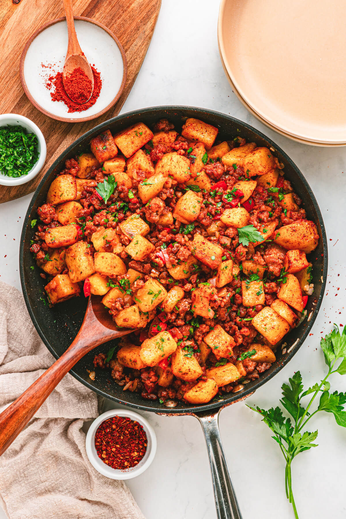 A cast iron skillet filled with vibrant papas con chorizo containing red peppers, potatoes, chorizo and cilantro as garnish.