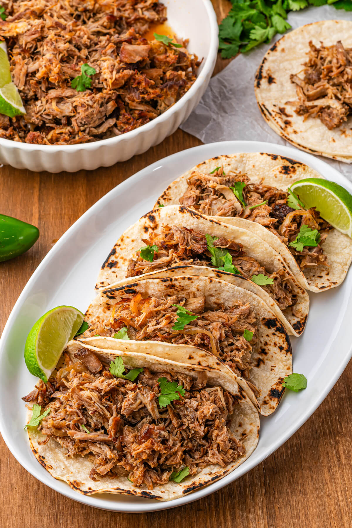 A platter of corn tortillas stuffed with juicy crispy pulled Slow Cooker Carnitas garnished with chopped cilantro and lime wedges.