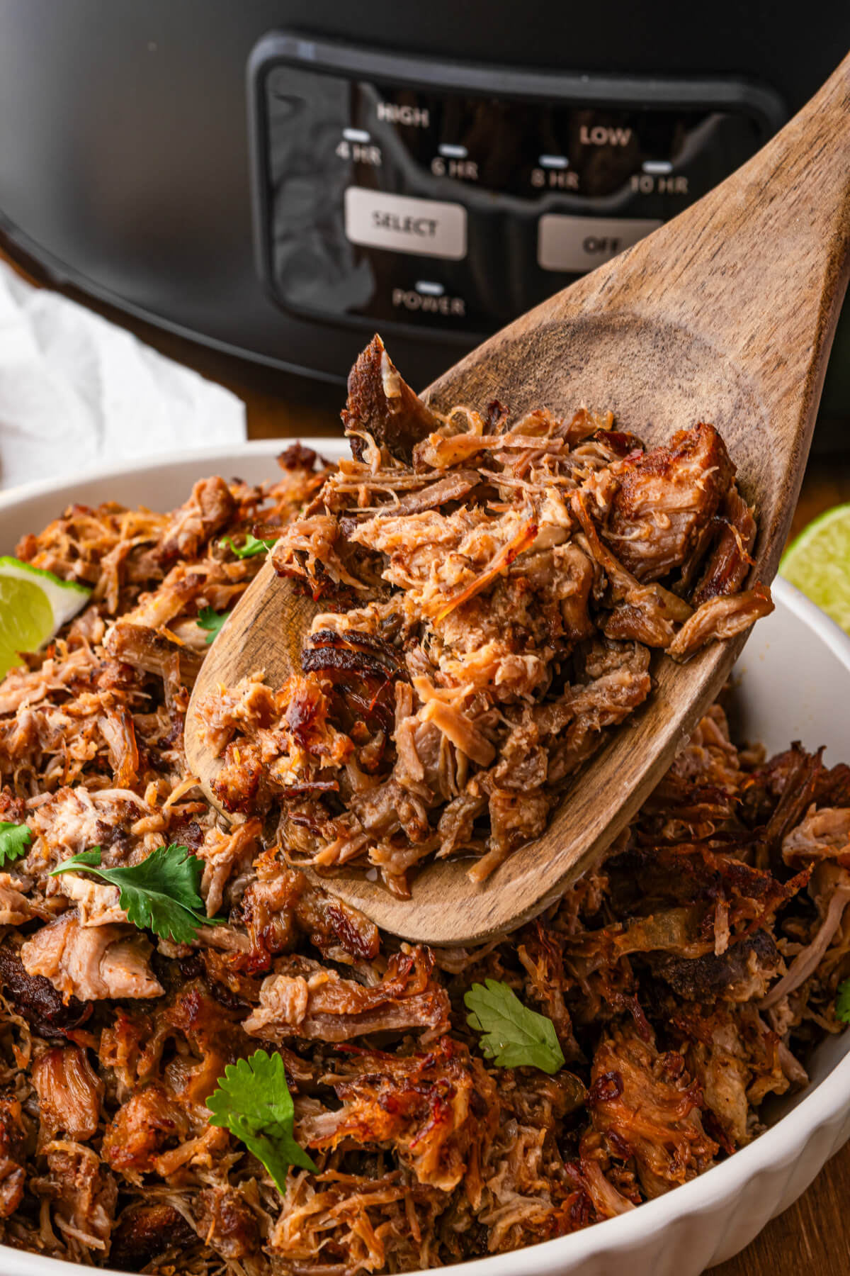 A wooden spoon dishing out slow cooker carnitas into a white bowl.
