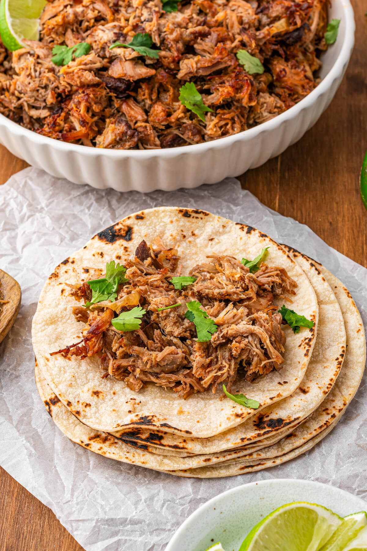 A stack of corn tortillas topped with pork carnitas garnished with chopped cilantro and lime.
