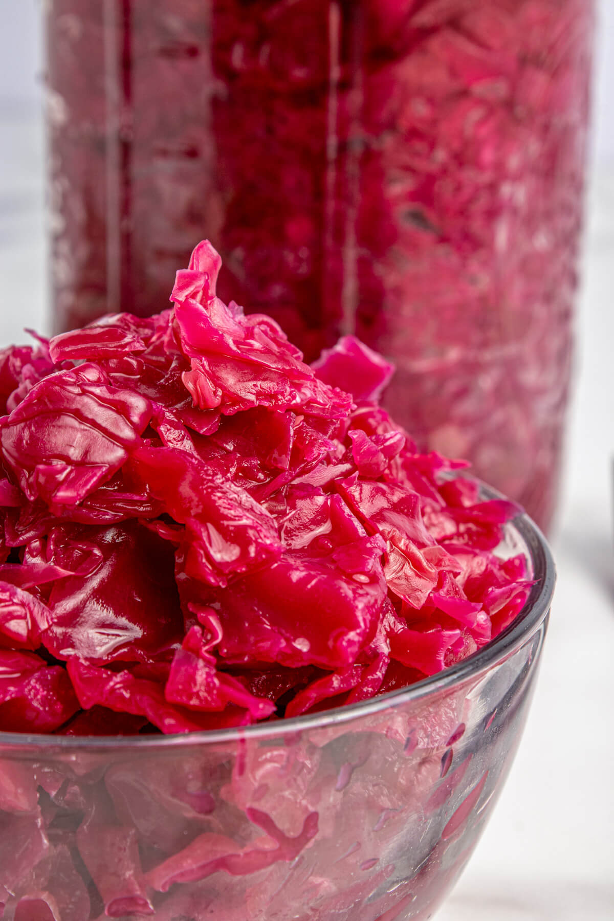 A glass bowl filled with vibrant purple fermented cabbage in front of a full jar of red cabbage sauerkraut. 