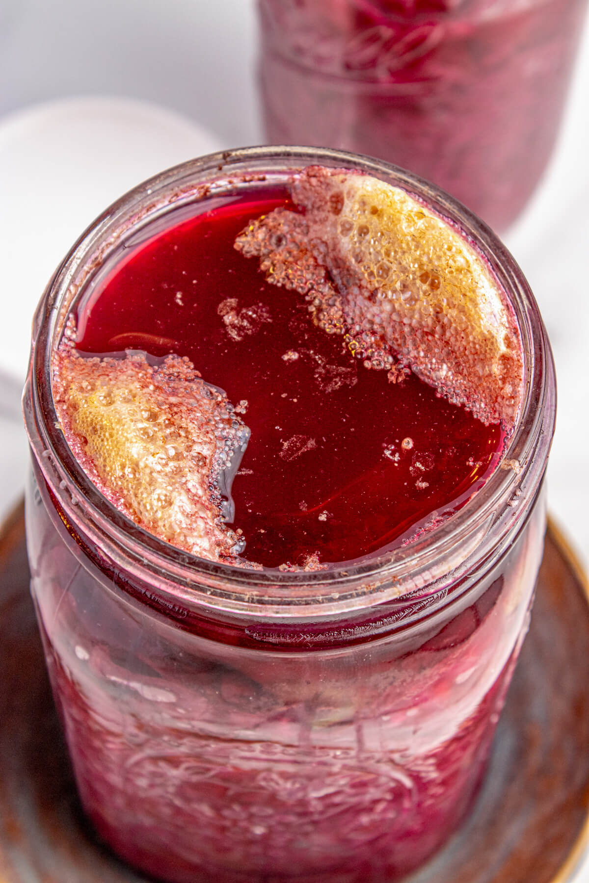 A glass jar filled with fermenting red cabbage topped with bubbly liquid.
