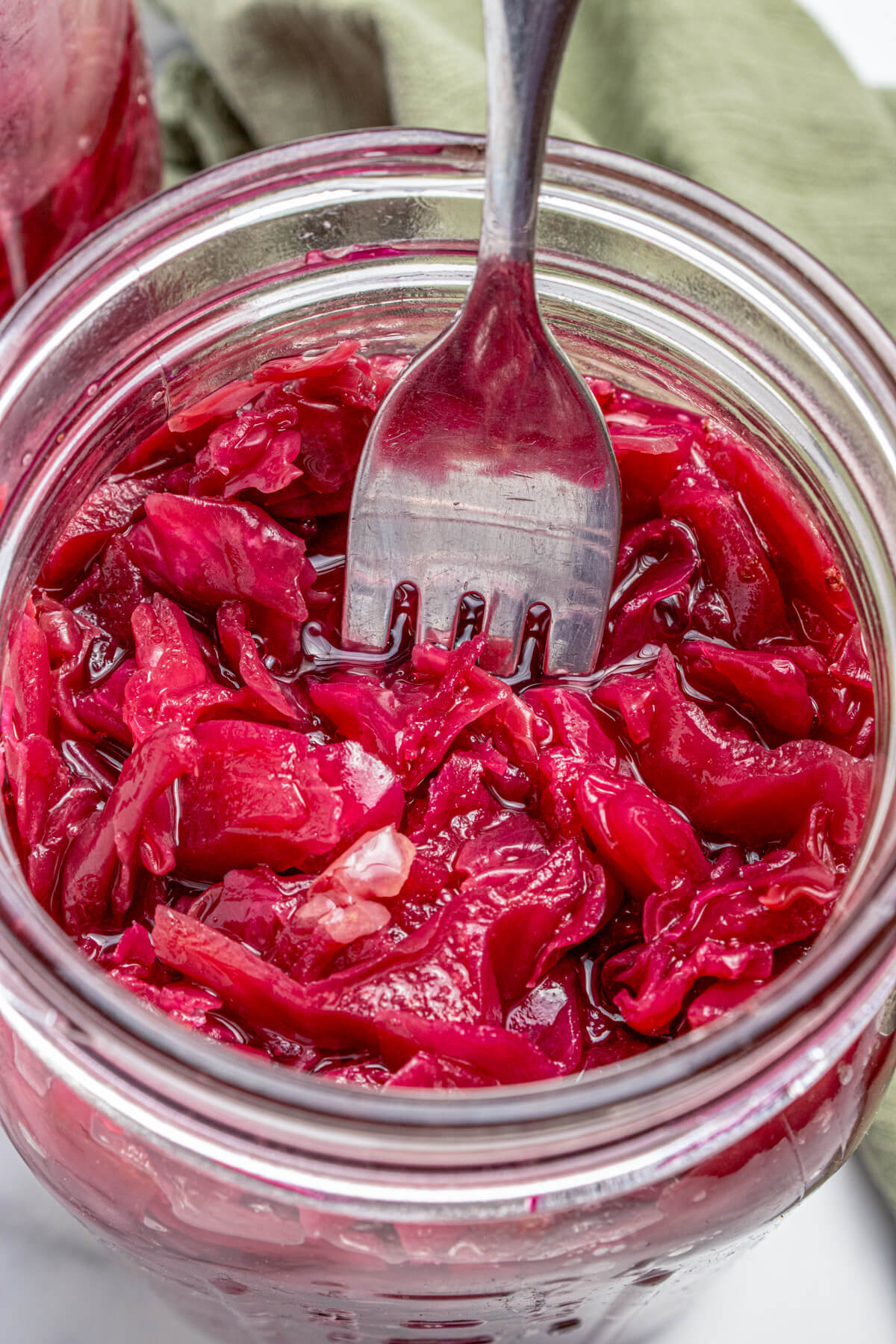 A fork in a glass jar filled with vibrant purple fermented cabbage.