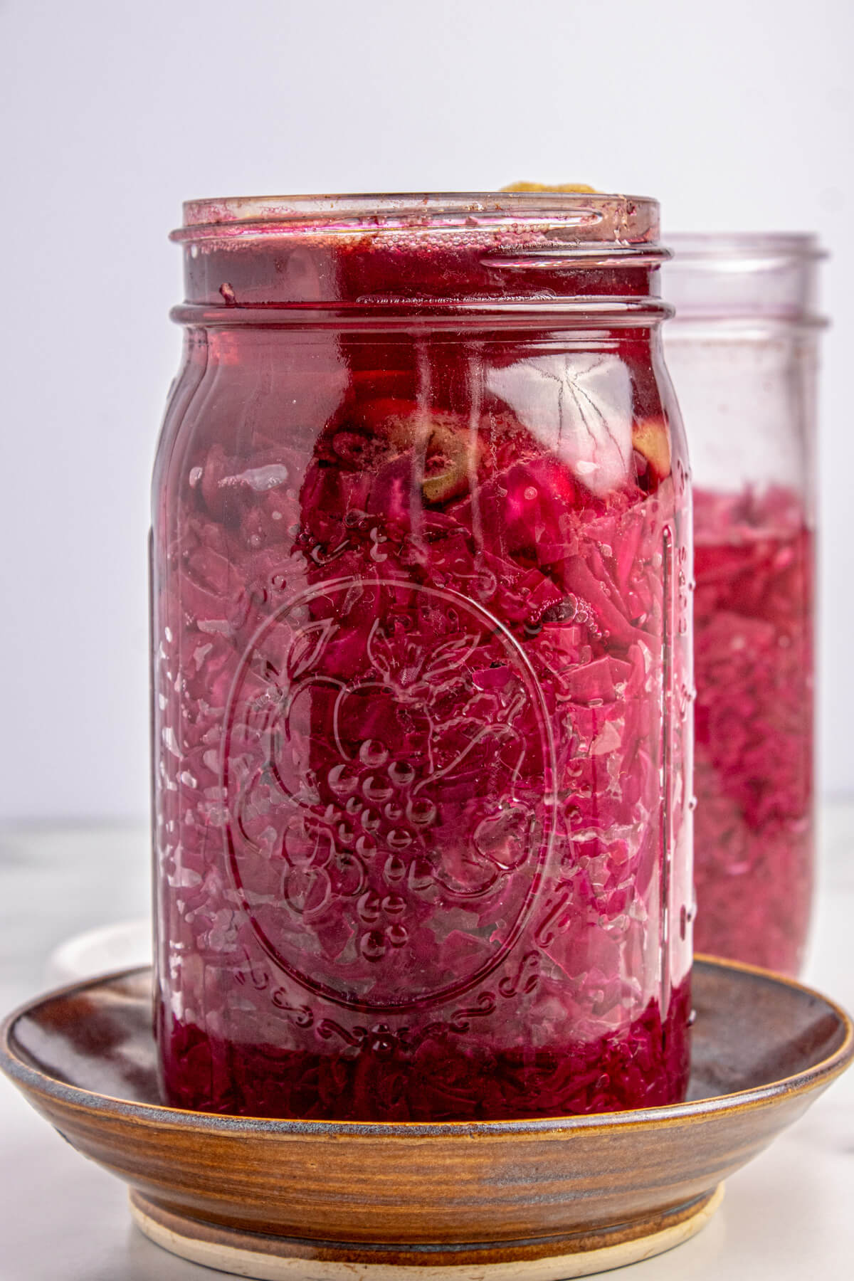 A glass jar filled with fermenting red cabbage topped with bubbly liquid.