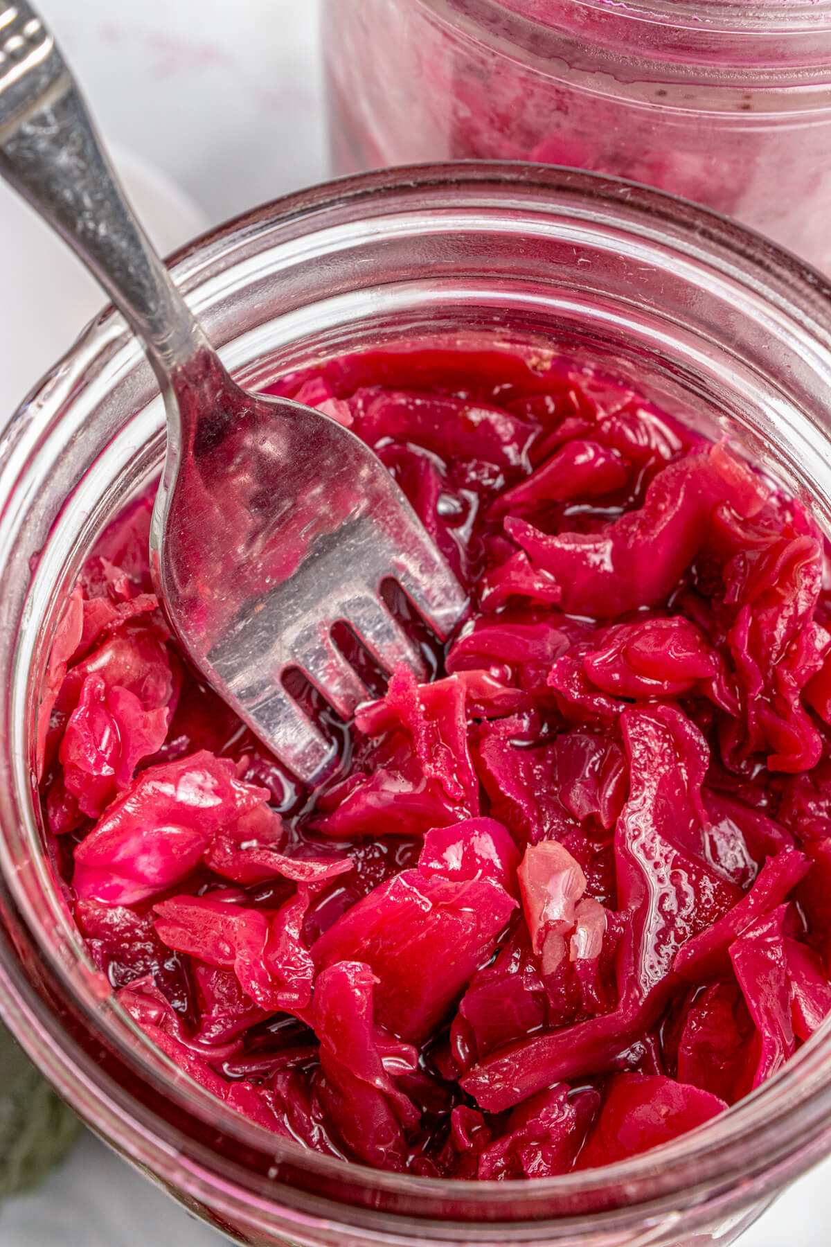 A fork in a glass jar filled with vibrant purple fermented cabbage.
