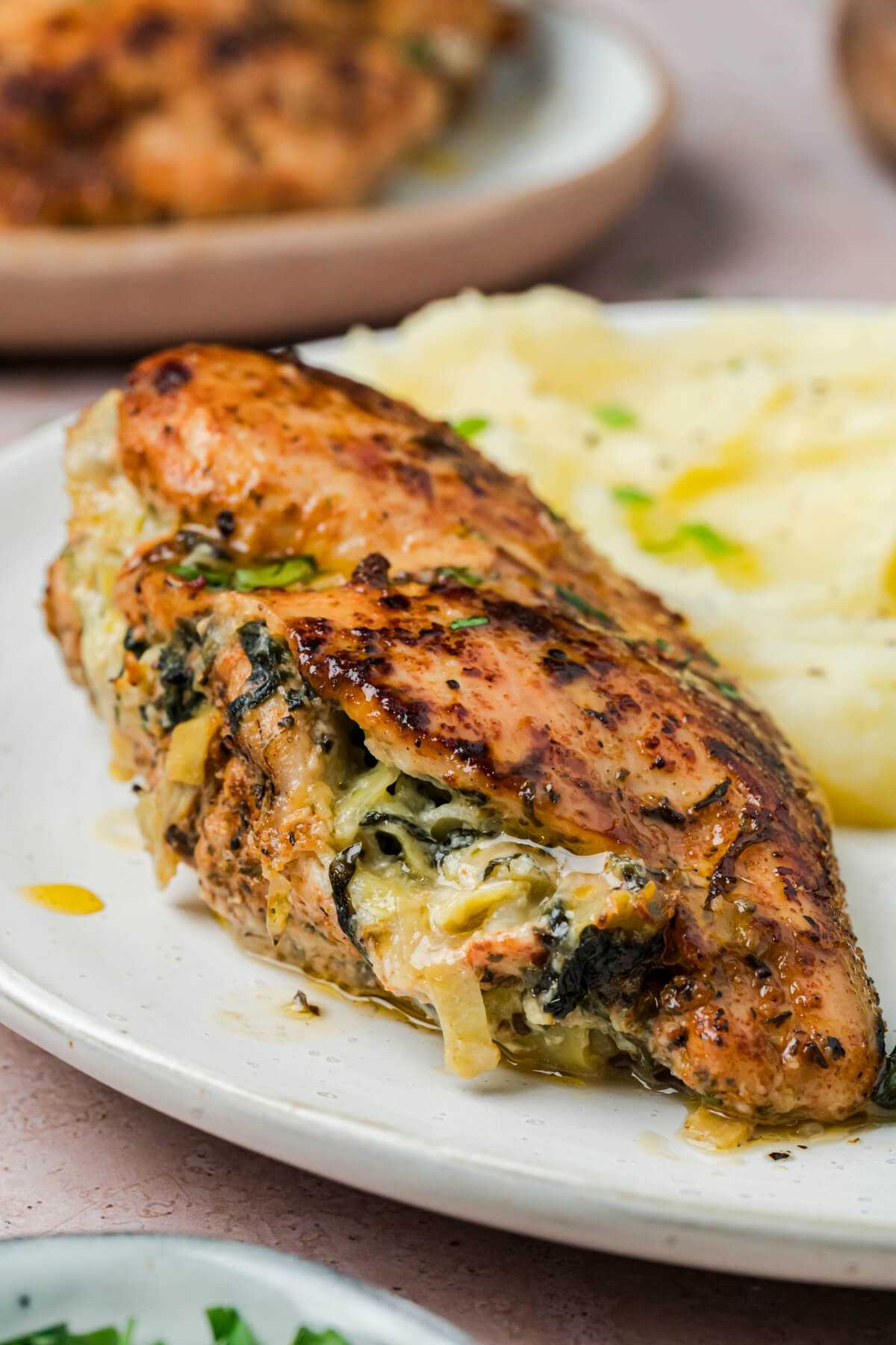 A dinner plate containing spinach artichoke stuffed chicken breast beside mashed potatoes.
