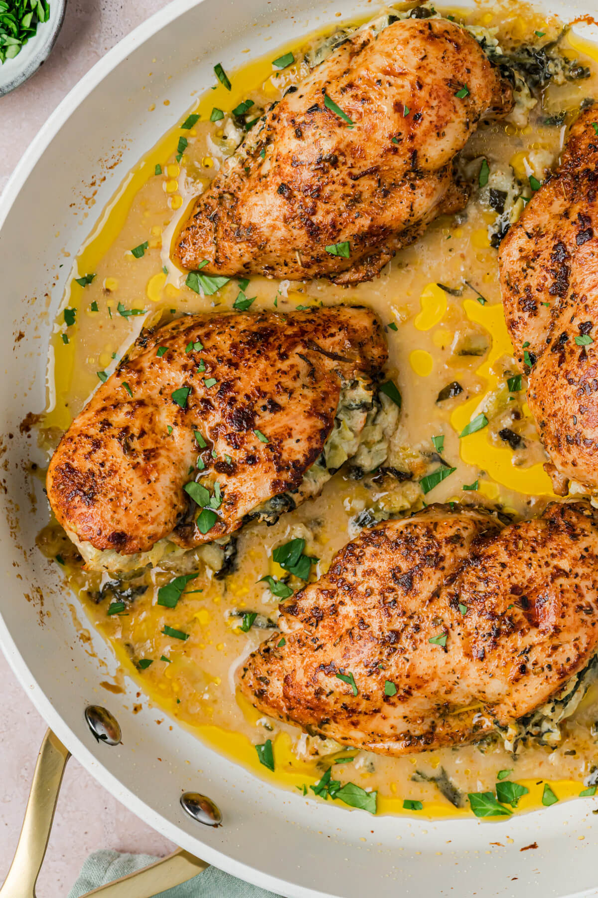 A white skillet containing four Spinach artichoke stuffed chicken breasts.