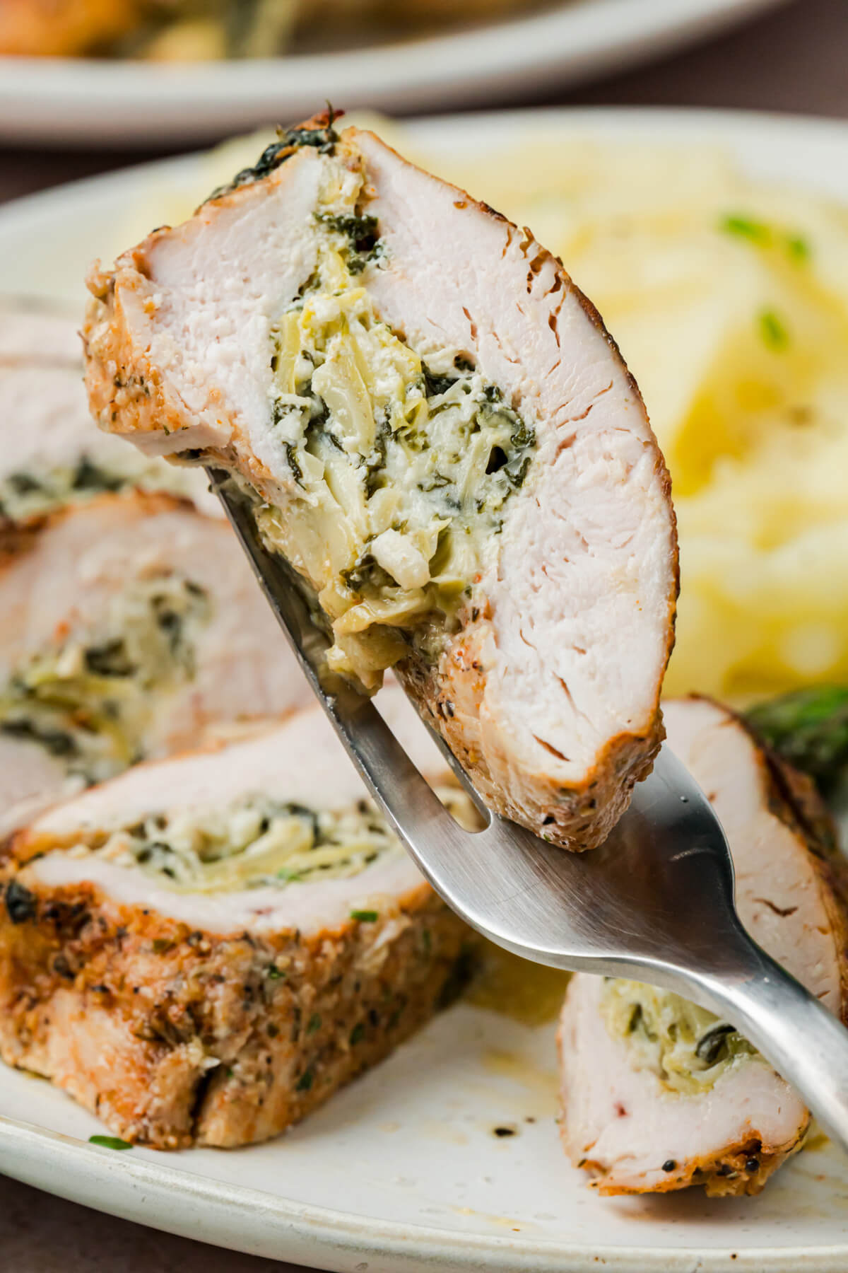 A fork containing a slice of spinach artichoke stuffed chicken.