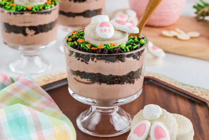 An individual Easter trifle featuring layers of cookie crumb dirt and chocolate whipped cream topped with a bunny butt cookie.