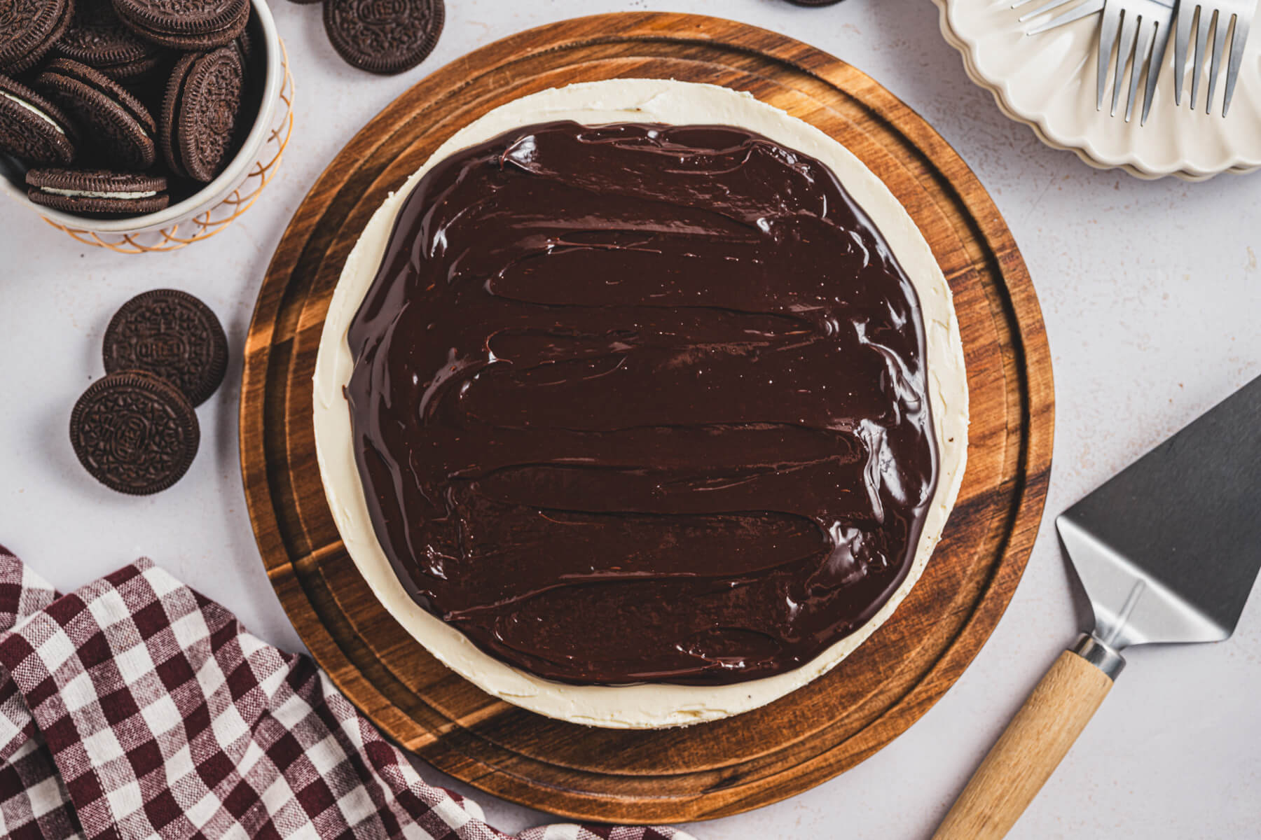 A whole no bake Bailey's Cheesecake topped with chocolate ganache on a wooden serving board.